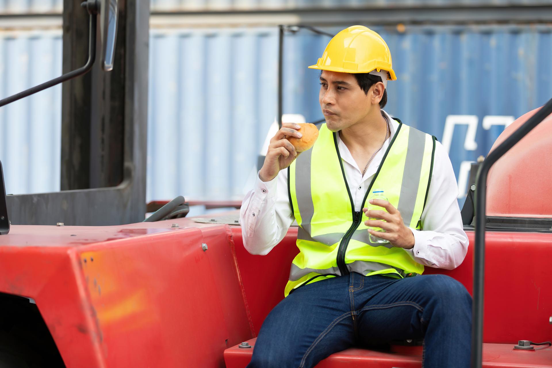 male factory worker or engineer eating bread during lunch break on truck in container warehouse storage